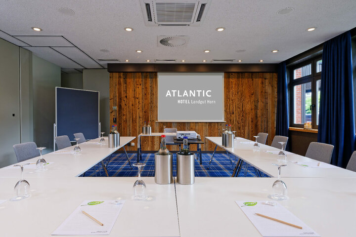 Modern conference room with U-shaped table, projector and wooden wall at the ATLANTIC Hotel Landgut Horn Bremen.