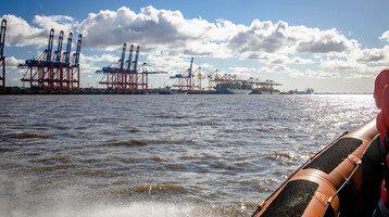 Blick vom Wasser auf Hafenkräne in Bremerhaven bei Sonnenschein, im Vordergrund ein Boot.