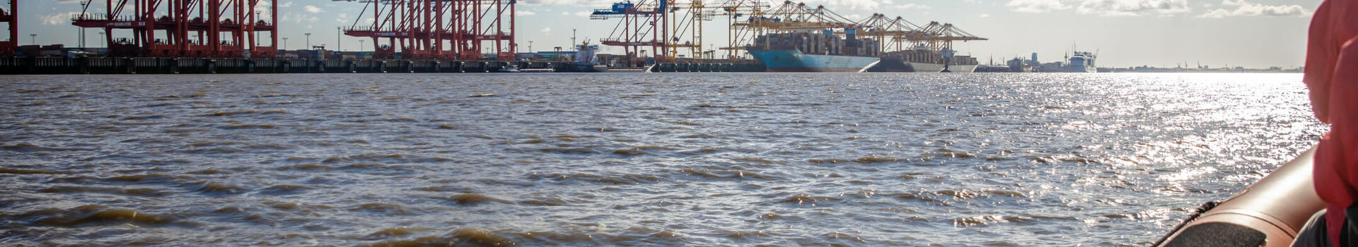 Blick vom Wasser auf Hafenkräne in Bremerhaven bei Sonnenschein, im Vordergrund ein Boot.