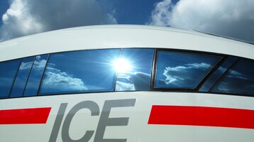 Close-up of an ICE train with reflective window and blue sky in the background.