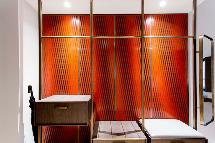 Modern hotel corridor with red, perforated walls, wooden cupboard, bench and umbrella stand.