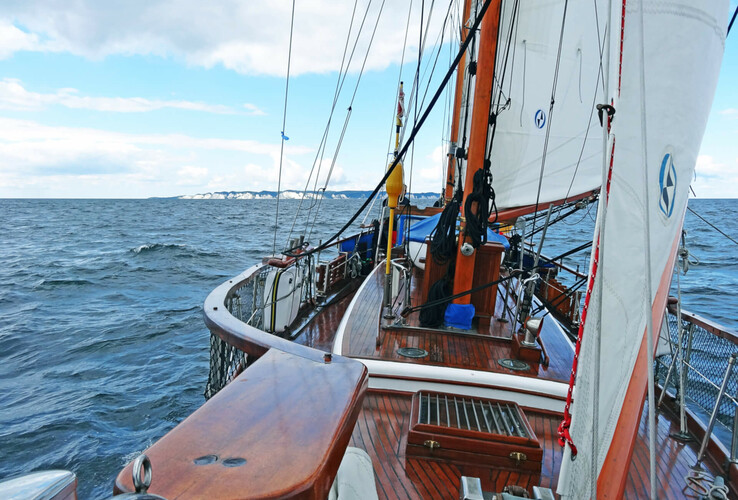 Segelboot auf der Ostsee mit Blick auf die Küste, unter blauem Himmel mit weißen Wolken.