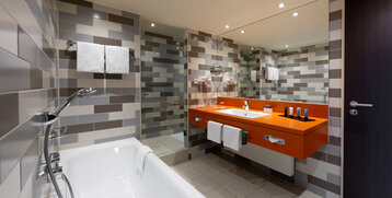 Modern bathroom with bathtub, orange washbasin, towels and patterned tiles at the ATLANTIC Hotel Bremen.