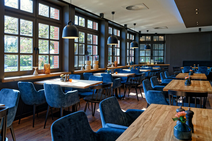 Restaurant VICTORIAN im ATLANTIC Hotel Landgut Horn Helles Restaurant mit großen Fenstern, Holztischen, blauen Polsterstühlen und moderner Beleuchtung im ATLANTIC Hotel.