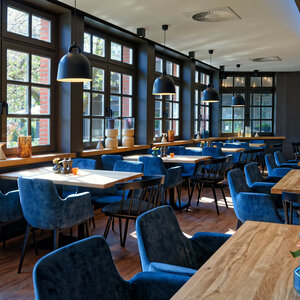 Helles Restaurant mit großen Fenstern, Holztischen, blauen Polsterstühlen und moderner Beleuchtung im ATLANTIC Hotel.