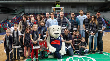 Pressemitteilung – ATLANTIC-Kids Eine Gruppe von Menschen posiert mit einem Eisbären-Maskottchen auf einem Basketballfeld.