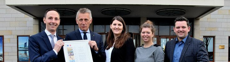 Fünf Personen posieren vor dem ATLANTIC Hotel Wilhelmshaven mit einer Auszeichnung.