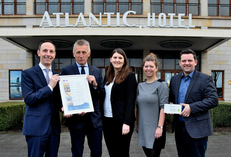 Fünf Personen posieren vor dem ATLANTIC Hotel Wilhelmshaven mit einer Auszeichnung.