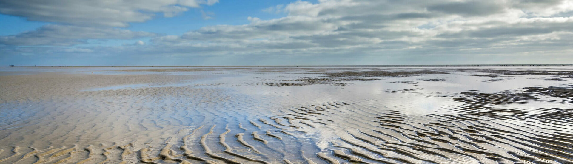 Extensive sandy beach at low tide with wave-like patterns, under a cloudy sky.