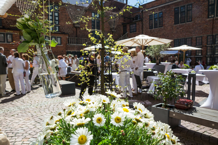 Social event in the sunny inner courtyard with flowers, guests in white and parasols at the ATLANTIC Grand Hotel Bremen.