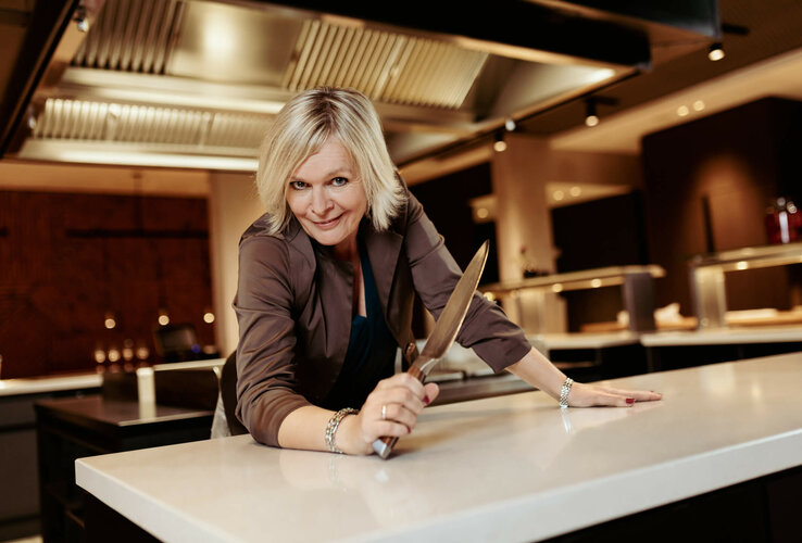cook in the modern kitchen of the ATLANTIC Hotel Münster, smiles and holds a knife on the work surface.