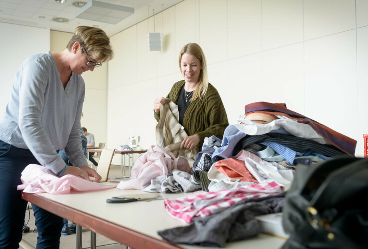 Zwei Frauen sortieren bunte Stoffe auf einem Tisch in einem hellen Raum des ATLANTIC Hotel Sail City.