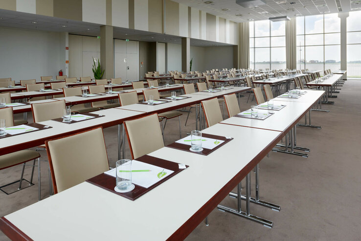 Bright conference room in the ATLANTIC Hotel Sail City with tables, chairs and a view of large windows.