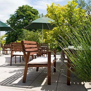 Sonnige Terrasse mit Holzmöbeln, grünen Pflanzen und Sonnenschirmen im ATLANTIC Hotel Vegesack, Bremen.