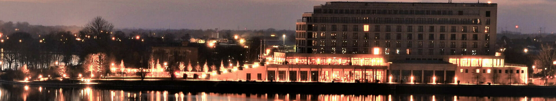 ATLANTIC Hotel Wilhelmshaven at dusk, illuminated, reflected in the calm waters of the harbor.
