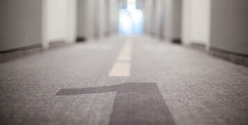 Flur im ATLANTIC Hotel Airport Bremen mit Teppichboden und zentraler Linie, Türen zu beiden Seiten, in Unschärfe.