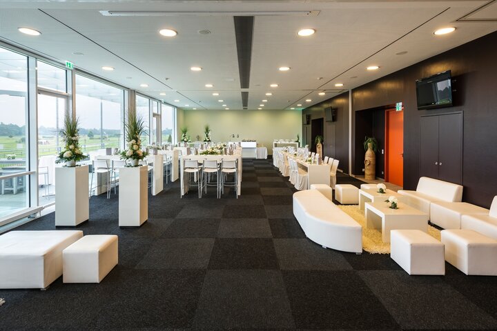 Alle Event-Räume bieten Ihnen einen schönen Blick ins Grüne direkt auf die Galopprennbahn Moderner Veranstaltungsraum im ATLANTIC Hotel mit weißen Möbeln, großen Fenstern und Blick auf die Galopprennbahn.