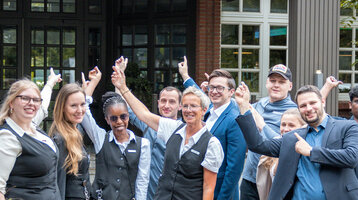 Hotelteam vor dem Eingang des ATLANTIC Hotel Landgut Horn Bremen, lächelnd und freundlich.