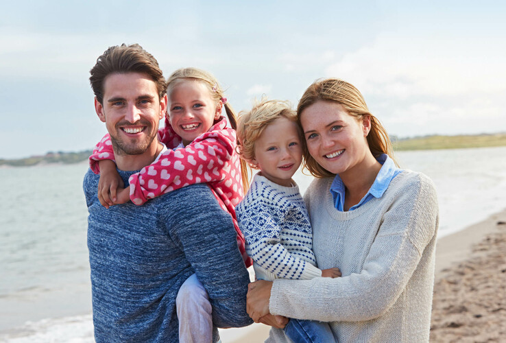 Family on the beach, smiling, with a view of the sea, in sunny weather. Ideal for a relaxing vacation.