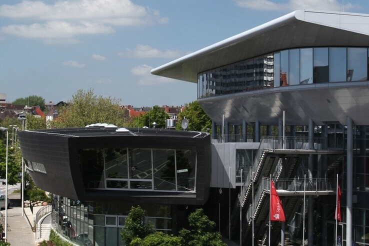 Modern building with glass façade, surrounded by trees, under a blue sky.