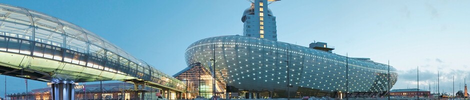 Futuristisches Gebäude des ATLANTIC Hotel Sail City in Bremerhaven, beleuchtet und am Wasser gelegen.