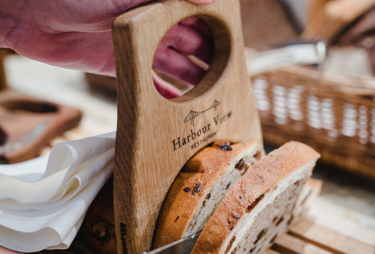 Hand cuts bread with wooden holder on cutting board.