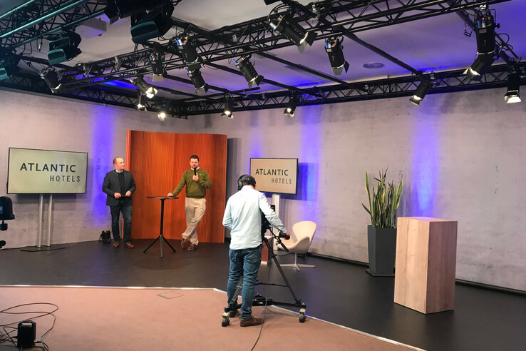 Zwei Männer auf einer Bühne mit Kameramann, umgeben von ATLANTIC HOTELS-Logos und moderner Beleuchtung.
