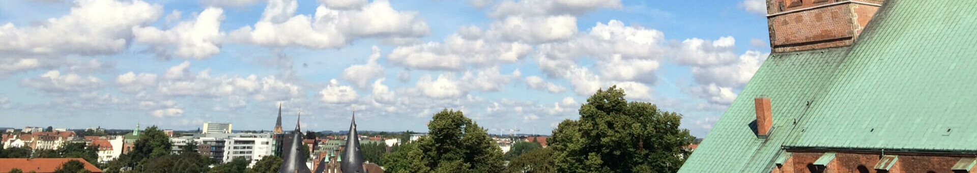 View from the Roof lounge | ATLANTIC Hotel Lübeck Church tower with green roof rises into blue sky with white clouds over Lübeck.