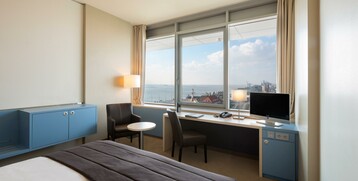 Bright hotel room with sea view, desk, chair and comfortable bed at the ATLANTIC Hotel Sail City, Bremerhaven.