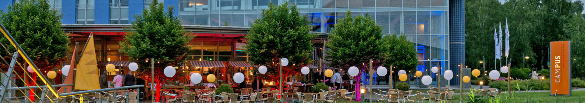 Außenansicht des ATLANTIC Hotel Universum, Bremen, mit beleuchteter Terrasse und blauer Fassade am Abend.