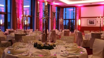 Elegantes Hotelrestaurant mit festlich gedeckten Tischen, Kerzenleuchtern und sanfter Beleuchtung in Rosa.
