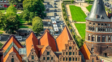 Historic city gate with brick buildings and red roofs, surrounded by green spaces and streets in a cityscape.