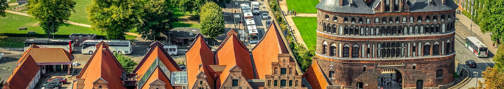 Historic city gate with brick buildings and red roofs, surrounded by green spaces and streets in a cityscape.
