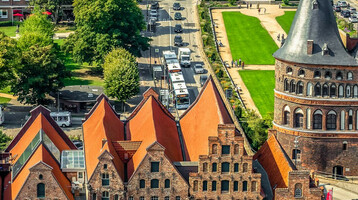 Historisches Stadttor mit Ziegelgebäuden und roten Dächern, umgeben von Grünflächen und Straßen in einer Stadtansicht.