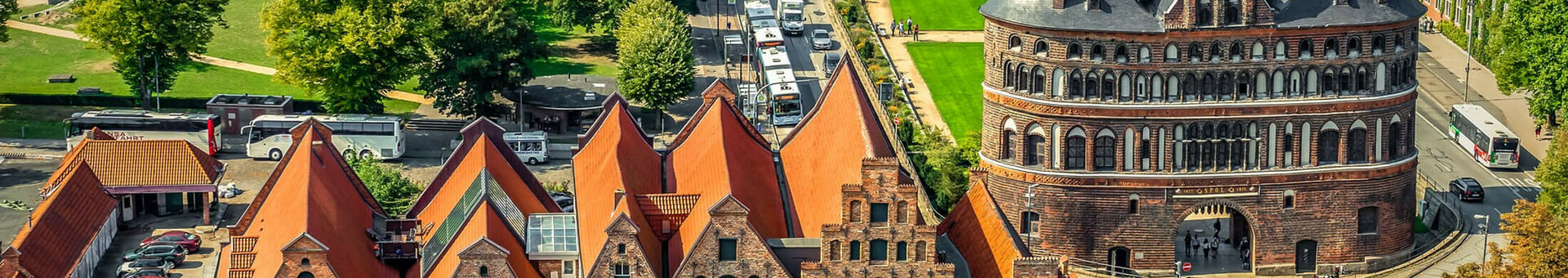 Historisches Stadttor mit Ziegelgebäuden und roten Dächern, umgeben von Grünflächen und Straßen in einer Stadtansicht.