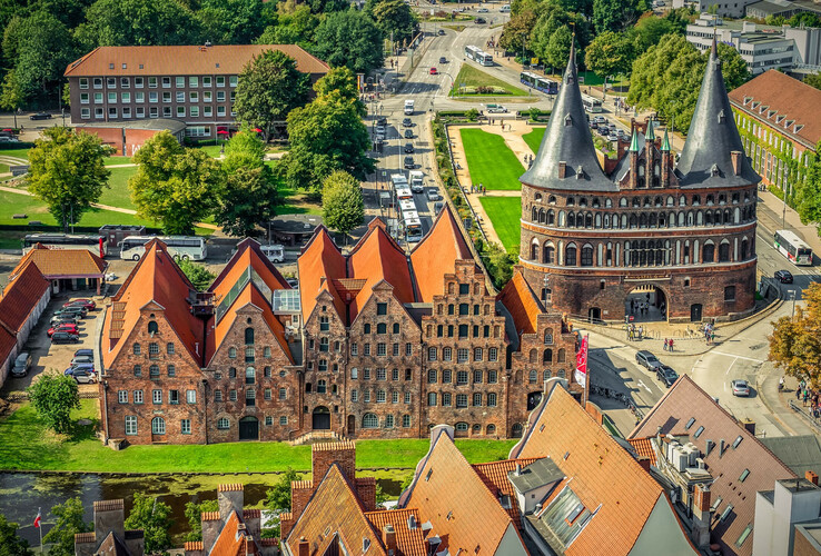 Historic city gate with brick buildings and red roofs, surrounded by green spaces and streets in a cityscape.