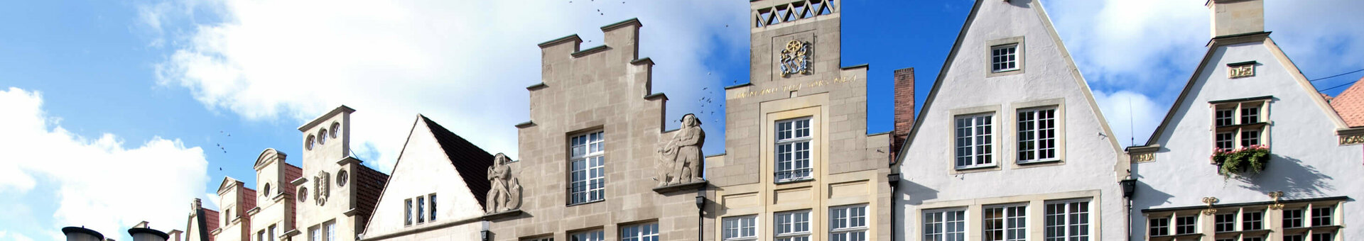 Historic facades on Prinzipalmarkt in Münster under a blue sky, with people and bicycles on the cobblestones.