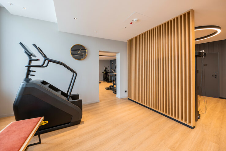 Moderner Fitnessraum im ATLANTIC Hotel Heidelberg mit Stepper, Holzwand und Wanduhren.