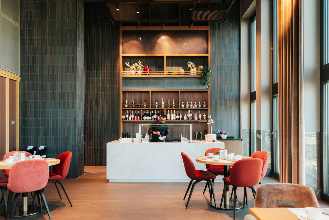ATLANTIC Hotel Heidelberg Breakfast Modern hotel restaurant with bar, red chairs, large windows and a bartender behind the counter at the ATLANTIC Hotel Heidelberg.