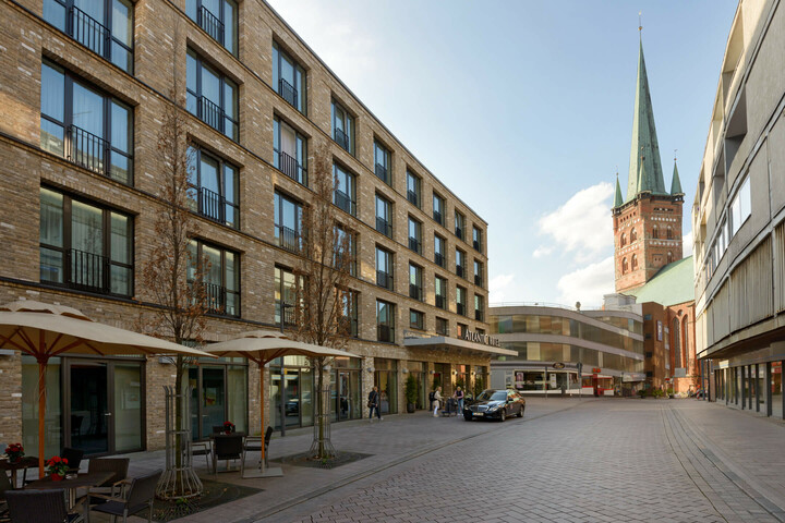 Exterior view of the ATLANTIC Hotel Lübeck with modern brick building and church tower in the background.