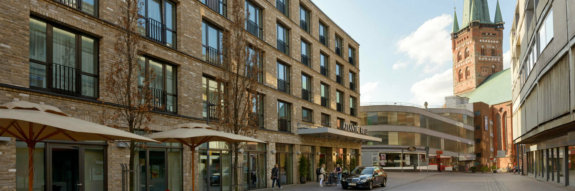 Exterior view of the ATLANTIC Hotel Lübeck with modern brick building and church tower in the background.