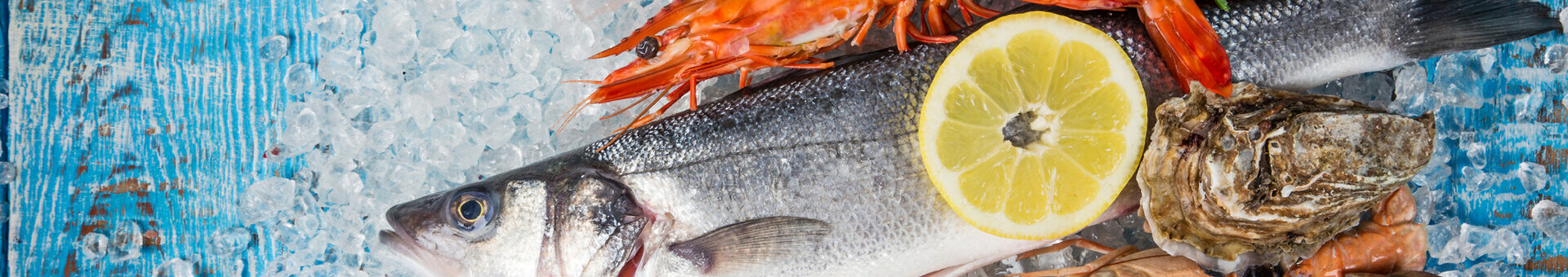 Frischer Fisch, Garnelen, Zitrone und Austern auf Eis, präsentiert auf blauem Holz.