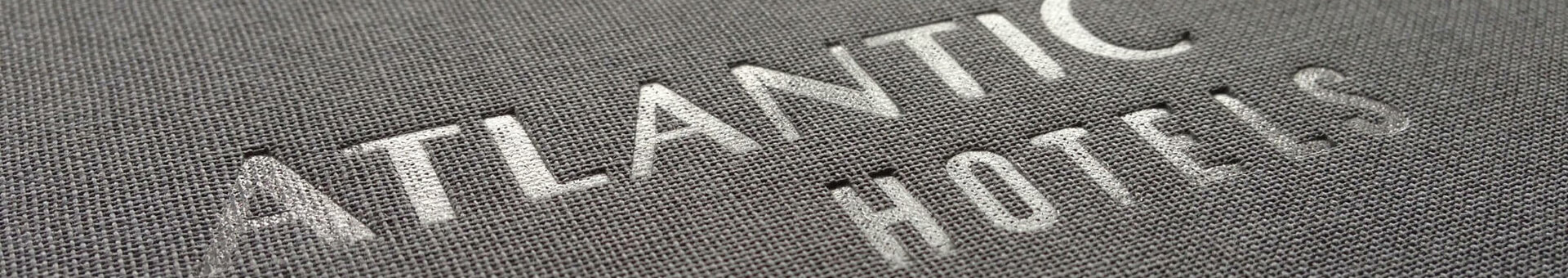 Embossed logo "Atlantic Hotels" on gray fabric surface.