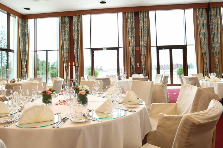 Eleganter Bankettsaal mit gedeckten runden Tischen, weißen Stühlen und großen Fenstern mit Blick auf die Terrasse.