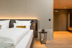 Modernes Hotelzimmer mit großem Bett, stilvollem Nachttisch, Blumen und sanfter Beleuchtung im ATLANTIC Hotel Heidelberg.