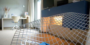 Modernes Hotelzimmer mit Schreibtisch, Stuhl, TV und stilvollem Metallstuhl im Vordergrund.