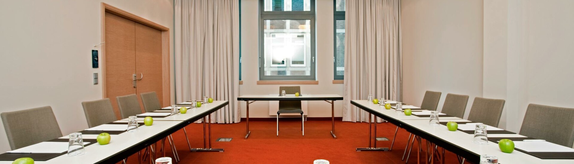 Moderner Konferenzraum mit U-förmiger Tischanordnung, grünen Äpfeln und Schreibmaterial, im ATLANTIC Hotel Kiel.