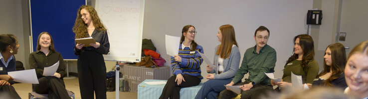 The trainees sit in a large circle of chairs while planning the trainee day.