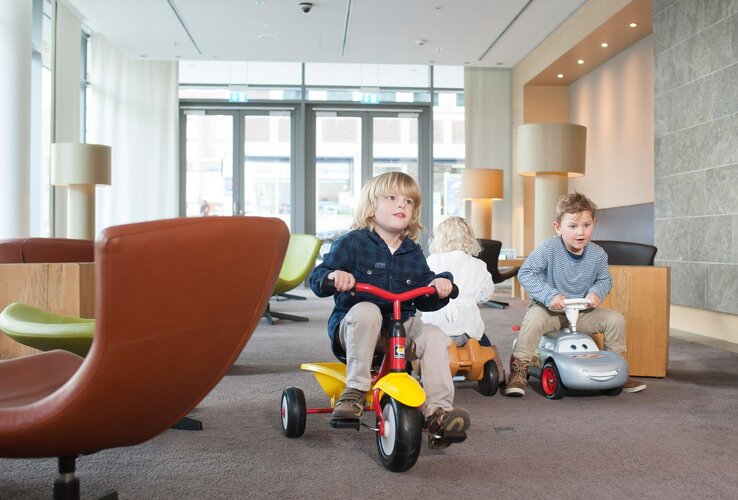 Kinder spielen auf Spielzeugfahrzeugen in der Lobby des ATLANTIC Hotels Kiel.