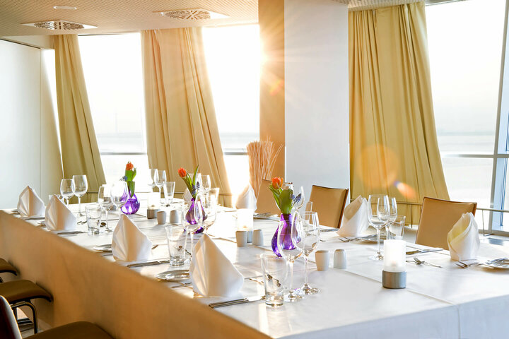 Elegant gedeckter Tisch in hellem Raum mit Meerblick im ATLANTIC Hotel Sail City, Bremerhaven.
